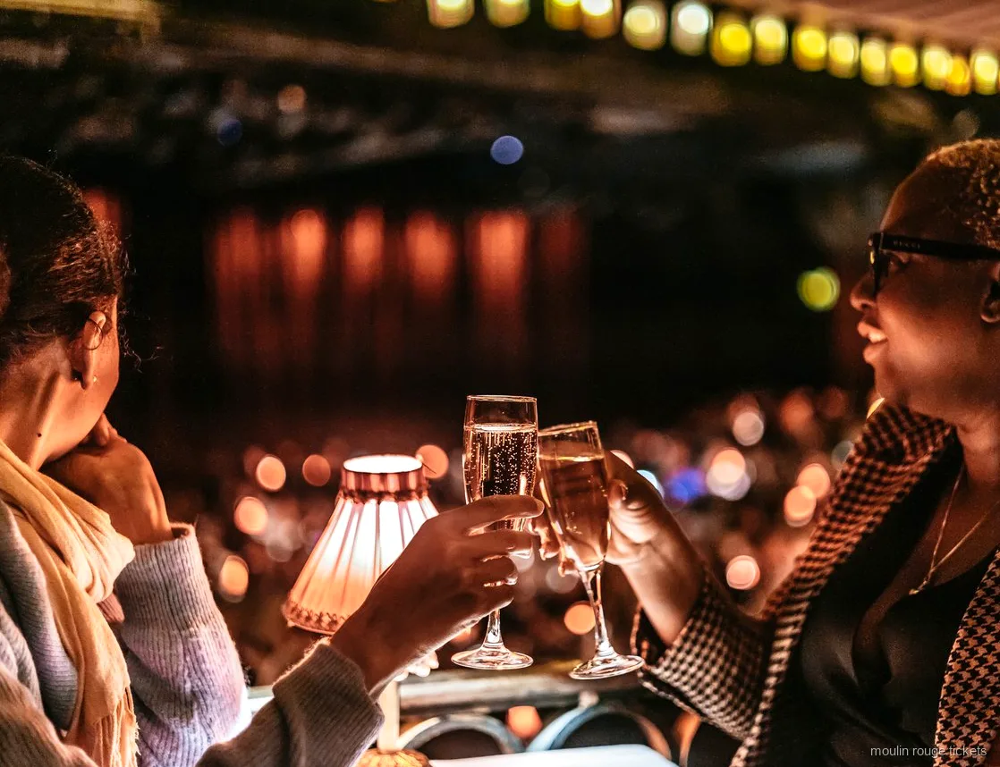 Duas convidadas brindam com champanhe junto a um abajur, bilhetes Moulin Rouge para o show da noite