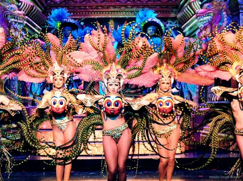 Danseuses aux ailes de plumes roses et rayées, masques dorés, sur un décor orné, dîner spectacle Moulin Rouge