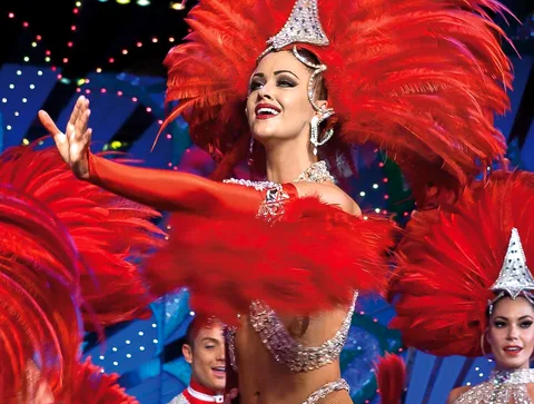 Entradas Moulin Rouge: bailarina con tocado de plumas rojas y lentejuelas bajo las luces del escenario