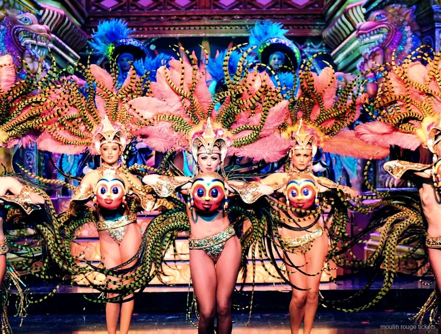 Dançarinas com asas de penas rosa e máscaras douradas em cenário ornamentado, jantar e show Moulin Rouge