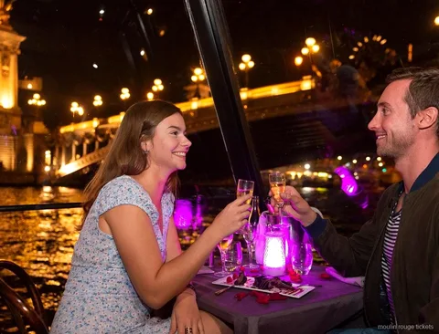 Casal brindando com champanhe num jantar em cruzeiro noturno pelo Sena, antes do show com bilhetes Moulin Rouge