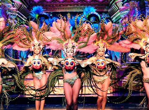 Tancerki z różowymi skrzydłami z piór i złotymi maskami na bogatej scenografii, bilety Moulin Rouge z kolacją