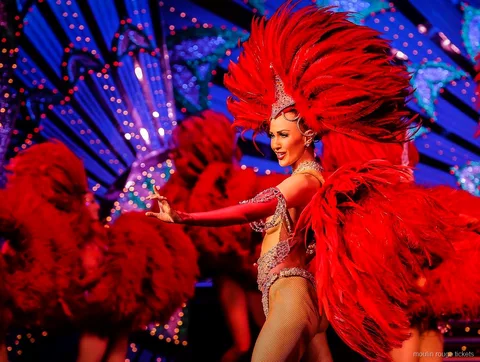 Mavi ışıklı dekorun önünde büyük kırmızı tüy yelpazeli dansçı, Moulin Rouge gösteri biletleri