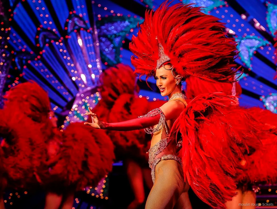 Mavi ışıklı dekorun önünde büyük kırmızı tüy yelpazeli dansçı, Moulin Rouge gösteri biletleri