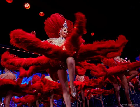暗いステージで大きな赤い羽根の扇を振りながら脚を高く上げて踊る羽根飾りの踊り子たち、ムーランルージュ ディナーショー チケット