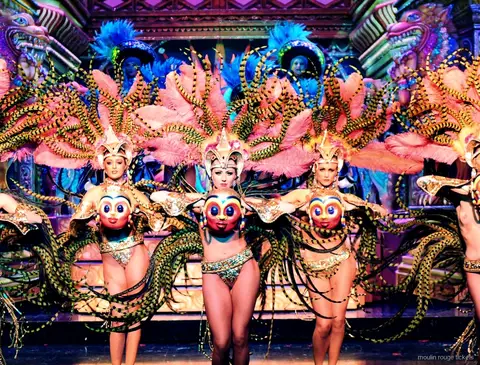 Dansere med lyserøde stribede fjervinger og gyldne masker foran en pyntet kulisse, Moulin Rouge dinner show
