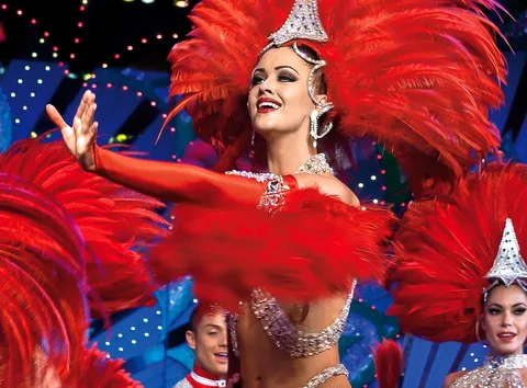 Moulin Rouge tickets: dancer in a red feather headdress and sequins reaching out under stage lights
