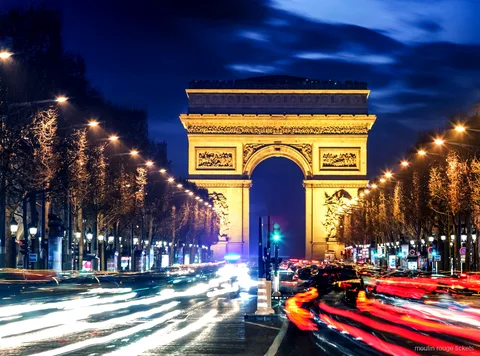 Beleuchteter Arc de Triomphe bei Nacht am Ende der Champs Élysées mit Lichtspuren, Route vor den Moulin Rouge Tickets