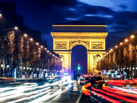 Arc de Triomphe lit up at night at the end of the Champs Élysées with traffic light trails, en route to Moulin Rouge tickets