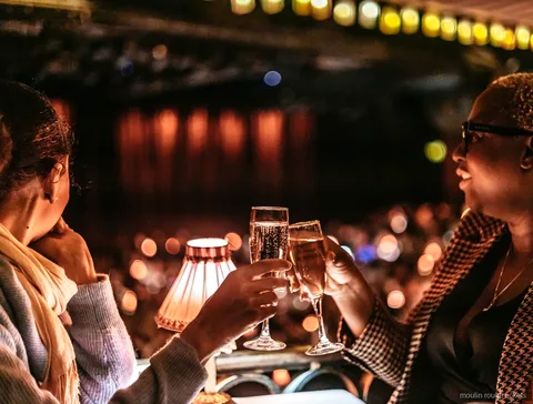 Zwei Gäste stoßen am Tisch mit Lampe mit Champagner an, Moulin Rouge Tickets für die Abendshow
