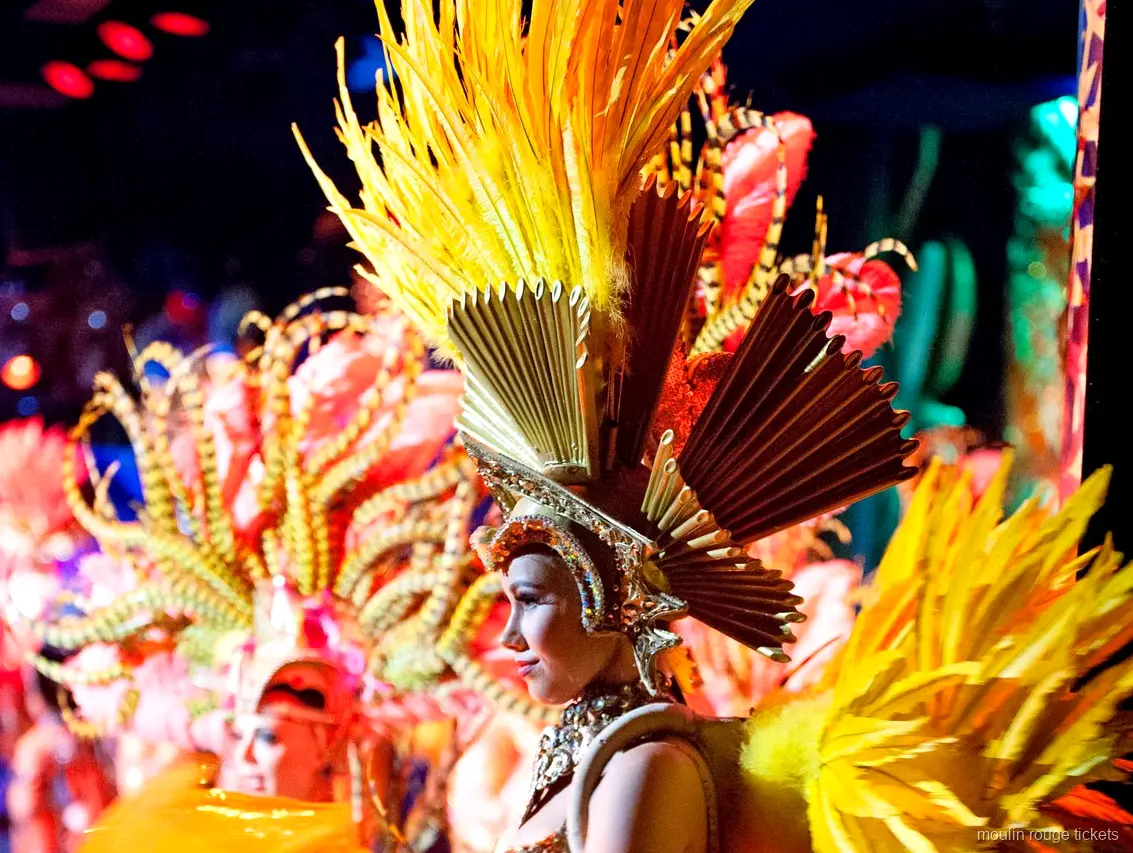Moulin Rouge biletleri: sahnede altın rengi tüylü başlık ve yelpaze taç takan dansçı