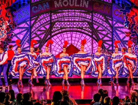 Ballarina de cancan en un salt d'espagat amb faldilla blava de volants i parella, sopar espectacle Moulin Rouge