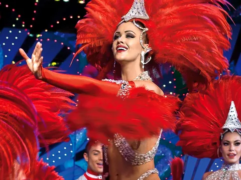 Billets Moulin Rouge : danseuse en coiffe de plumes rouges et paillettes sous les lumières de la scène
