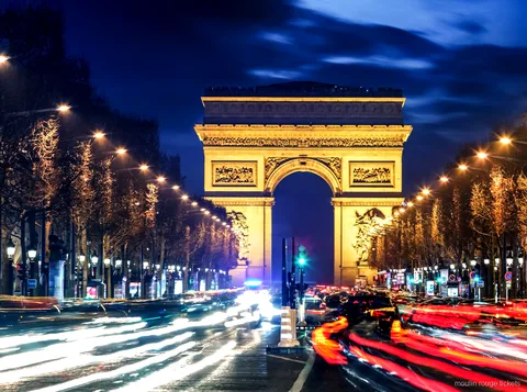 Arc de Triomphe illuminé la nuit au bout des Champs Élysées avec traînées lumineuses, avant les billets Moulin Rouge